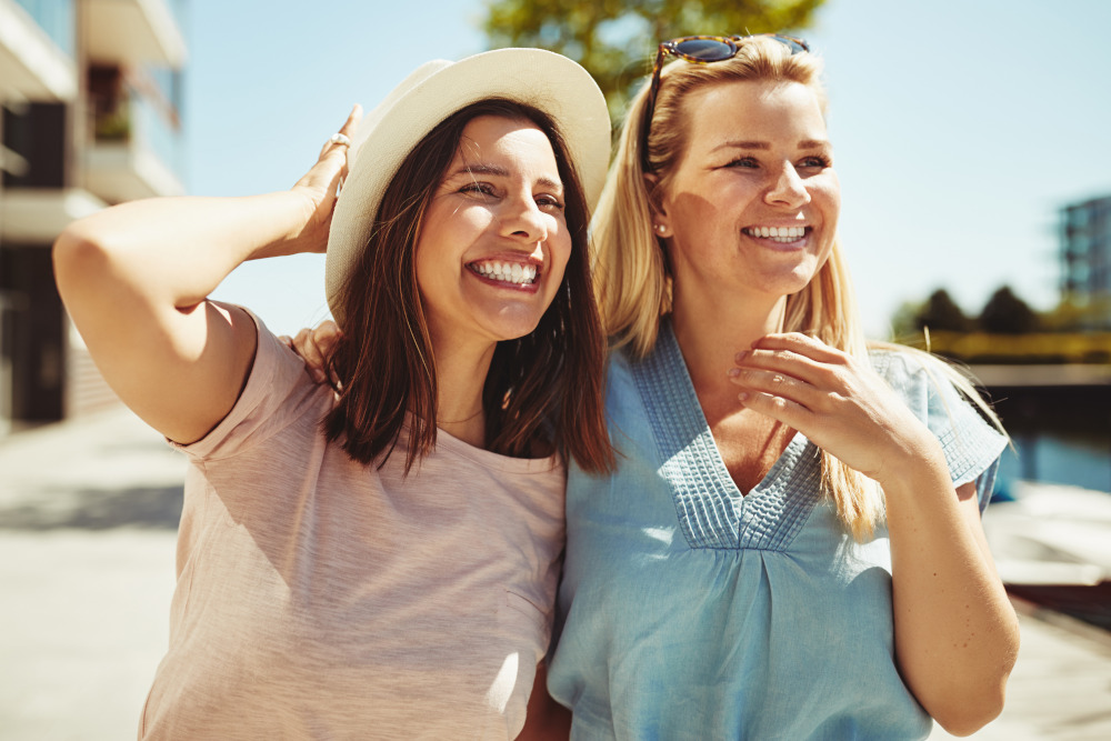 Two laughing young female friends having a good time walking together on sunny day in the city.