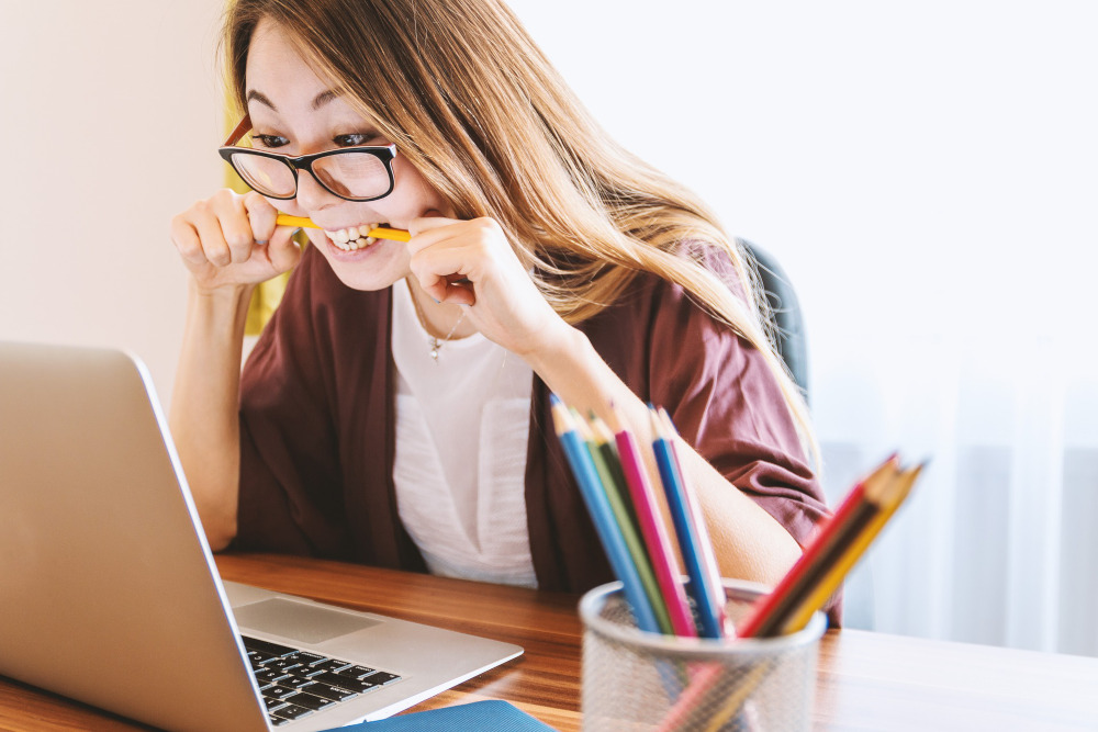 Young woman studying on a computer while biting a pencil.
