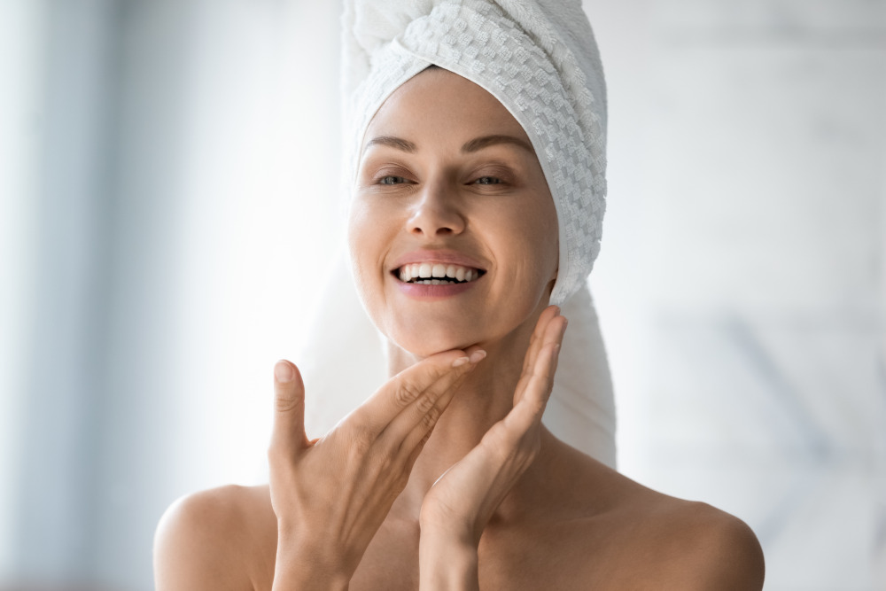 How long do profound result last? Happy woman with her hair wrapped in a towel looking at her face in the bathroom mirror.